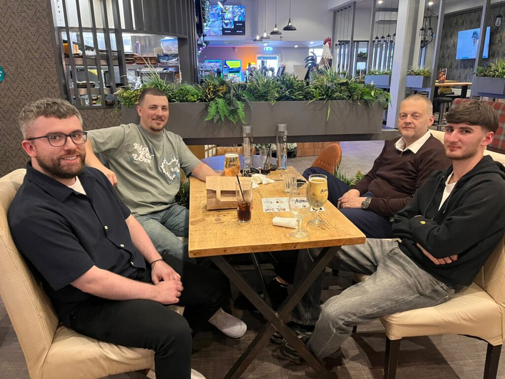 Four people from CMT Engineering sitting around a wooden table Six smiling people from CMT Engineering sitting around a wooden table at the Cherrywood Smokehouse Bar & Grill